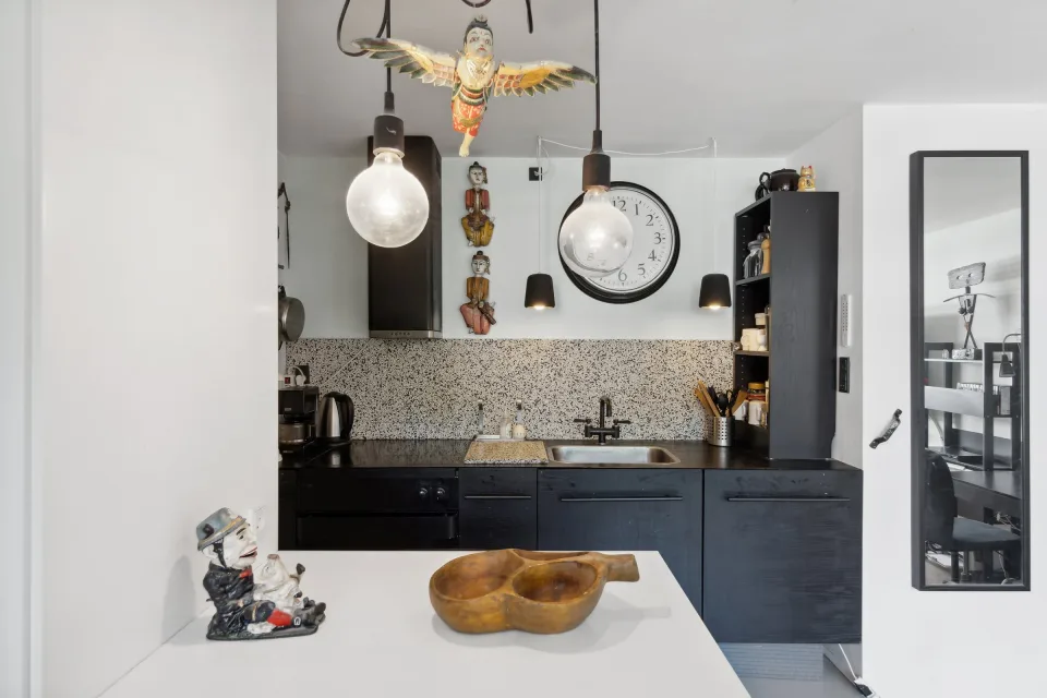 Det gamle køkken med sortmalede fronter, terrazzo-stænkplade, stålvask og pendler over bordpladen.