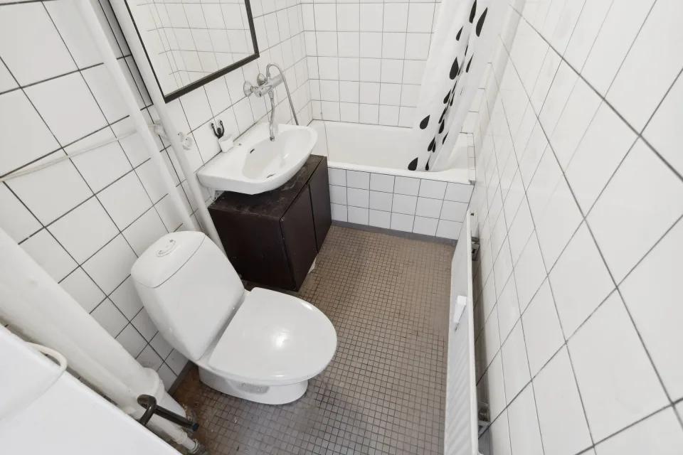 Toilet og håndvask på et mørkt skab i det gamle badeværelse med badekar ved siden af.