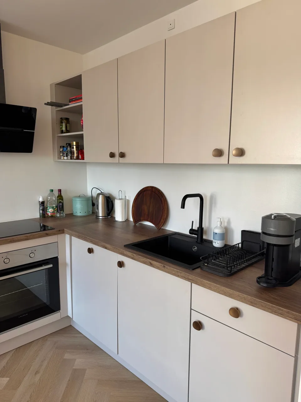 Køkkenbordplade i træ med sort granitvask, sort armatur og åbne hylder over — set i dagslys.