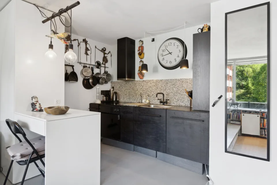 Køkkenvæggen før renovering med sorte skabe, granitbordplade og en emhætte i rustfrit stål.